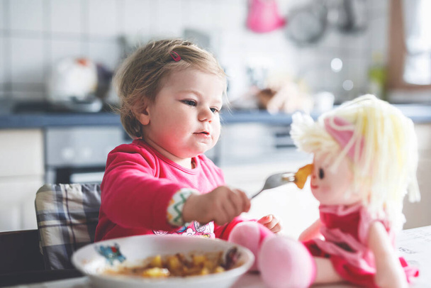 Adorable baby girl eating from fork vegetables and pasta. food, child, feeding and development concept. Cute toddler, daughter with spoon sitting in highchair and learning to eat by itself - Fotó, kép