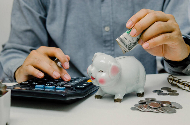 Hand man person holding dollar and calculator saving in pig bank. business finance economy investment tax accounting money and coin deposit concept. - Photo, image