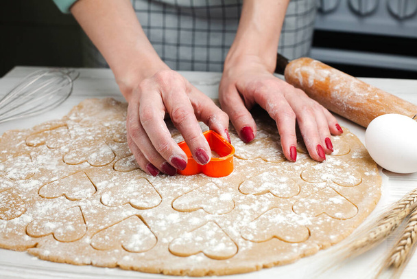 Naisen kädet leikkaa sydämiä taikinasta kotona keittiössä. Kotileivonnaisia. Ruoanlaitto prosessi. lähikuva. - Valokuva, kuva