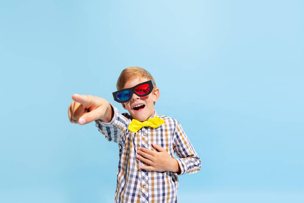At comedy movie. Emotional preschool boy, kid wearing retro style outfit and 3d glasses isolated on light blue background. Concept of child emotions, facial expression, fashion and ad. - Foto, Imagen