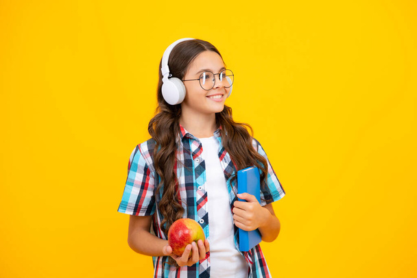 Back to school. Teenager schoolgirl with bag hold apple and book, ready to learn. School children on isolated yellow background - Fotografie, Obrázek