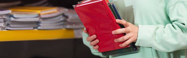 cropped view of child holding colorful copybooks in stationery store, banner  - Fotografie, Obrázek