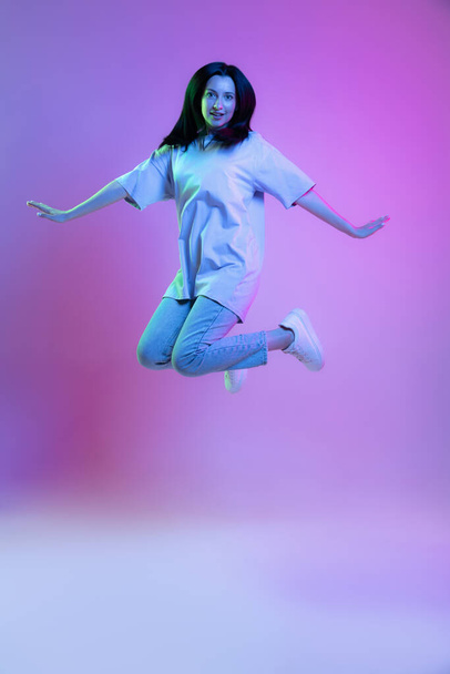 Portrait of adorable girl, young woman with long glossy dark hair isolated on purple background in neon light. Concept of beauty, art, fashion, youth, sales and ads. - Fotó, kép