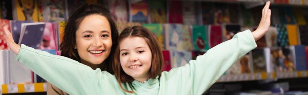 cheerful woman and excited girl with outstretched hands looking at camera in stationery store, banner - Foto, Imagem