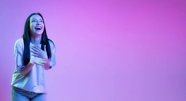 Laughing. Portrait of adorable girl, young woman with long glossy dark hair isolated on purple background in neon light. Concept of beauty, art, fashion, youth, sales and ads. - 写真・画像