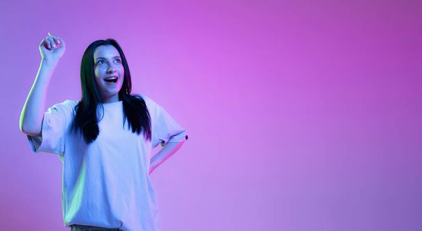 Having ideas. Portrait of adorable girl, young woman with long glossy dark hair isolated on purple background in neon light. Concept of beauty, art, fashion, youth, sales and ads. - Foto, Imagem