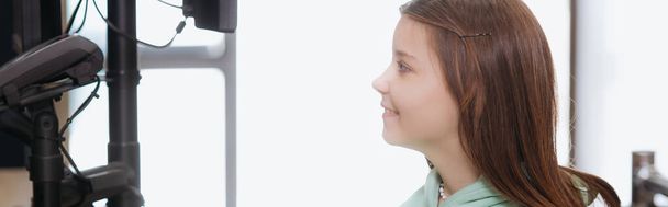 side view of smiling girl looking at payment terminal in shop, banner - Foto, afbeelding