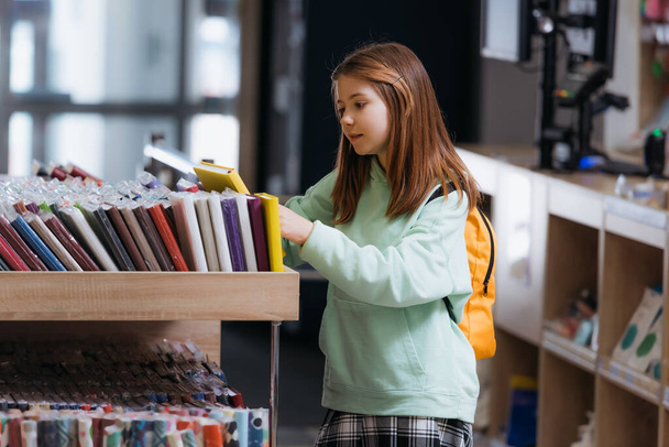 schoolgirl choosing from variety of copybooks in stationery store - Fotó, kép