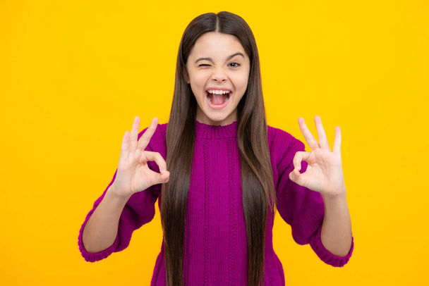 Portrait of a little teenager child girl showing okay gesture and winking isolated over yellow background. Ok sign concept. Excited face. Amazed expression, cheerful and glad - Valokuva, kuva