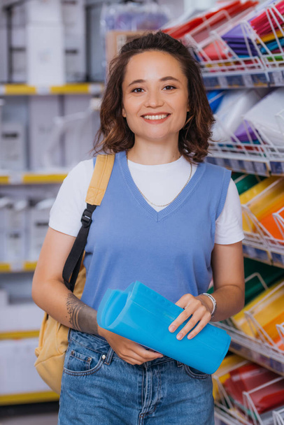 happy young woman with plastic files and backpack looking at camera in stationery store - Fotoğraf, Görsel