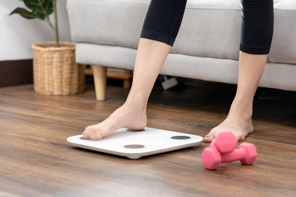 Ноги жінки наступають на електронні ваги, вимірюють вагу вашого тіла після тренування або сеансу йоги, контроль ваги, охорони здоров'я, вправи Дамбелла, фон світло-коричневе дерево зерно
. - Фото, зображення