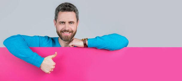 Man face portrait, banner with copy space. presenting novelty information. male behind pink paper show thumb up - Foto, afbeelding