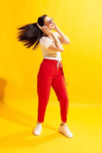 Dancing. Young beautiful woman in summer casual style outfit isolated on bright yellow background. Concept of beauty, art, fashion, youth, healthy lifestyle. Copyspace for ads, text, sales offer. - Фото, изображение