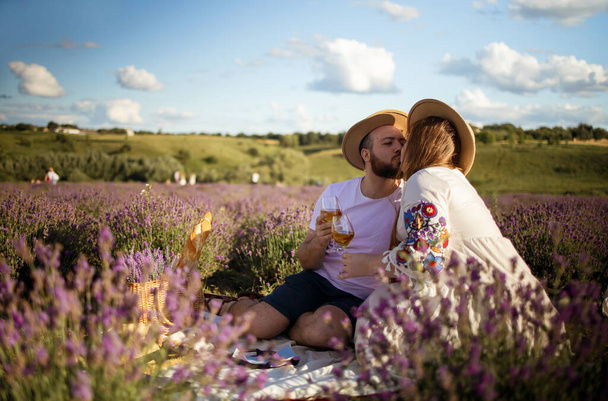 Man and woman hold glasses with white wine on background of a lavender field. Romantic picnic in sunset.  - Φωτογραφία, εικόνα