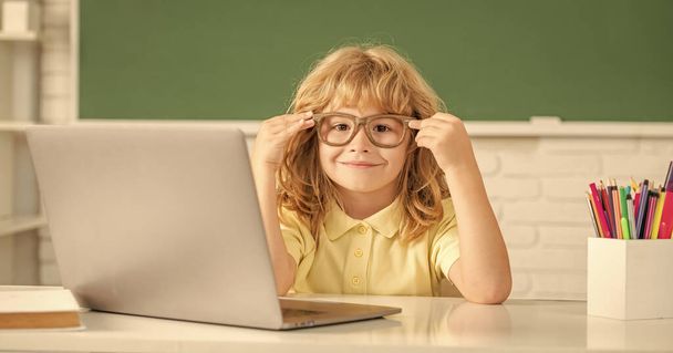 9月ラップトップで学校の教室でオンラインで勉強している陽気な子供の男の子. - 写真・画像