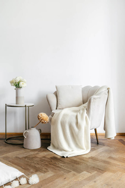 Mesa de café com flores perto de poltrona bege com travesseiro e xadrez. Design moderno da sala de estar com decoração de casa e mobiliário novo no apartamento - Foto, Imagem