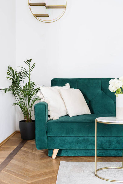 Boho design of living room with emerald velours couch, white cushions, coffee table with flower in ceramic vase and potted houseplant on the floor, closeup - Φωτογραφία, εικόνα
