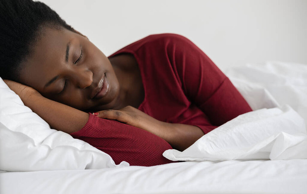 Young beautiful African woman sleeping in white linen bed, wearing red pajamas. - Foto, Imagen