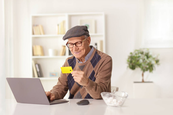Cheerful elderly man paying with a credit card on a laptop computer at home - Fotoğraf, Görsel