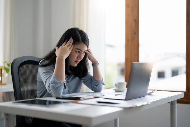Stresli iş kadını evde bir masada otururken dizüstü bilgisayarda çalışıyor ve elini şakaklarına koyup migren krizi geçiriyor. Serbest çalışmak, evden çalışmak. - Fotoğraf, Görsel