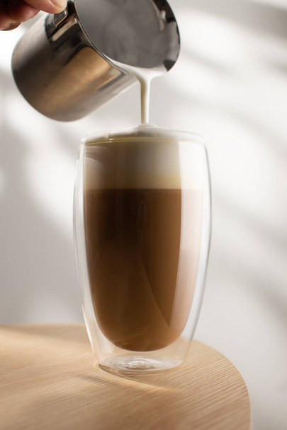 Cappuccino σε γυάλινο κύπελλο σε ξύλινο τραπέζι, Καφές και αφρό γάλακτος. - Φωτογραφία, εικόνα