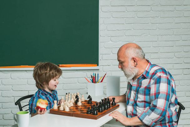 Grandfather and grandson boy playing chess, men generation. Different ages, grandfather and child grandson study chess together in home classroom - Valokuva, kuva