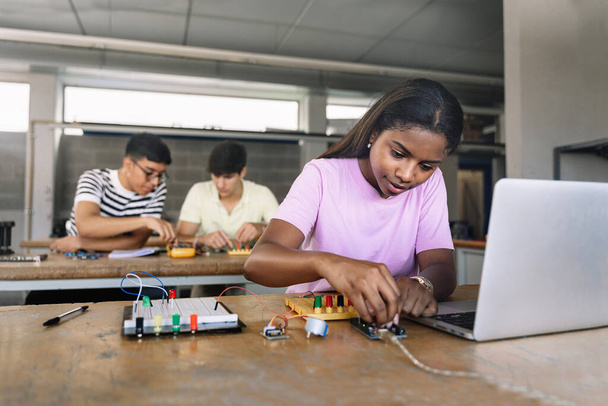 African American High School teenage Student programming electronics circuit board in the science technology workshop - Learning Digital Innovation in Education - 写真・画像