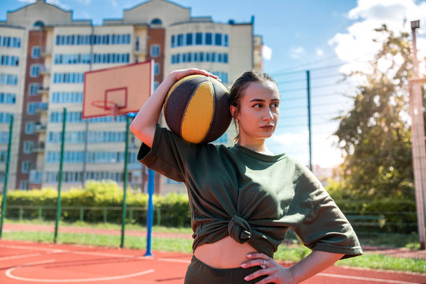 Junge hübsche kaukasische Frau hält Basketball auf Basketballplatz am Outdoor-Aktiv-Wochenende - Foto, Bild