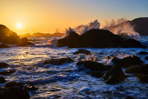 Image of Waves crashing over boulders on ocean during sunset - Foto, Bild