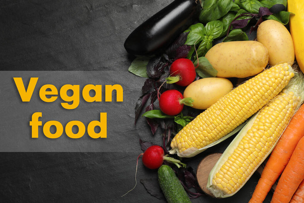 Phrase Vegan Food and fresh vegetables on black background, top view - Foto, afbeelding