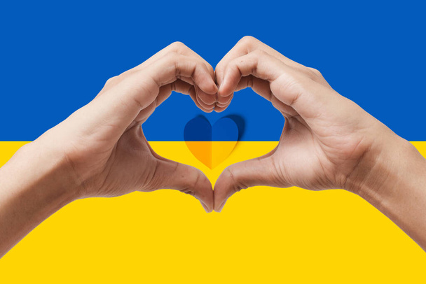 Man hands making a heart shape on Ukraine flag color background. Stay with ukraine symbol. Hand heart love gesture with ukrainian flag background. - Photo, Image