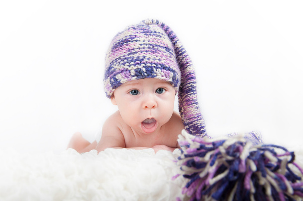 Νεογέννητο μωρό σε πολύχρωμα αστείο καπέλο μακρά, εξετάζοντας τη φωτογραφική μηχανή - Φωτογραφία, εικόνα