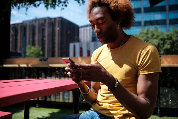 Портрет молодого небинарного человека с мобильного телефона и сидящего на столе в летний день. Внешний портрет. - Фото, изображение