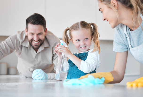 Happy family cleaning the kitchen together. Little girl spraying disinfectant from a bottle. Caucasian family cleaning the kitchen counter together. Mother and father bonding with their daughter. - Foto, Imagen