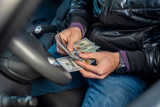 mains du conducteur de voiture mâle tenant de nouveaux billets de dollar au milieu de l'intérieur de la voiture. Concept d'entreprise. - Photo, image