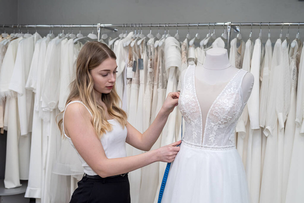 жіночий кравець використовує міру для вимірювання нової весільної сукні на манекені в магазині
 - Фото, зображення