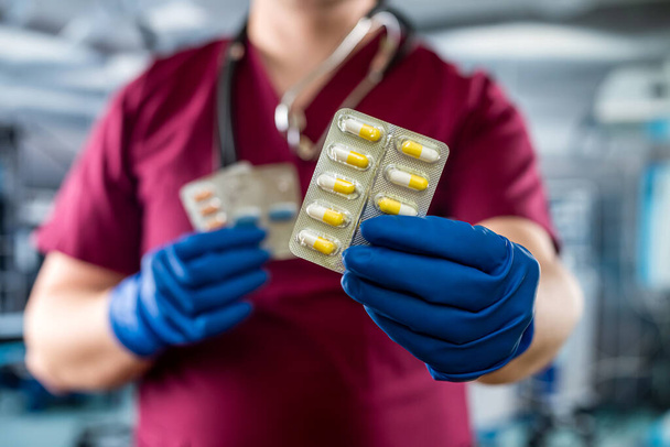 Mężczyzna lekarz trzymający opakowanie różnych tabletek w pokoju szpitalnym. Koncepcja leczenia chorób - Zdjęcie, obraz