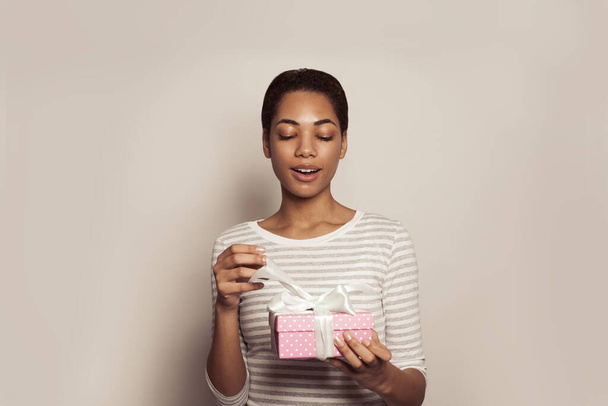 Muotokuva nuori afrikkalainen amerikkalainen nainen avaa läsnä laatikko valkoinen nauha. Onnellinen naismalli vaaleanpunainen lahja. - Valokuva, kuva