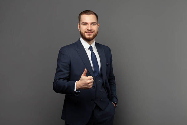 Joyful business man showing thumb up and looking at camera against grey studio wall banner background - Fotografie, Obrázek