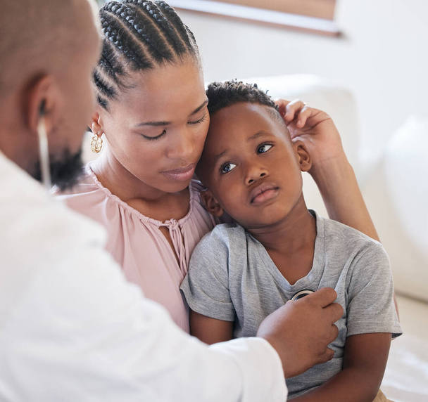 African american male paediatrician examining sick boy with stethoscope during visit with mom. Doctor checking heart lungs during checkup in hospital. Sick or sad boy receiving medical care. - Foto, Bild