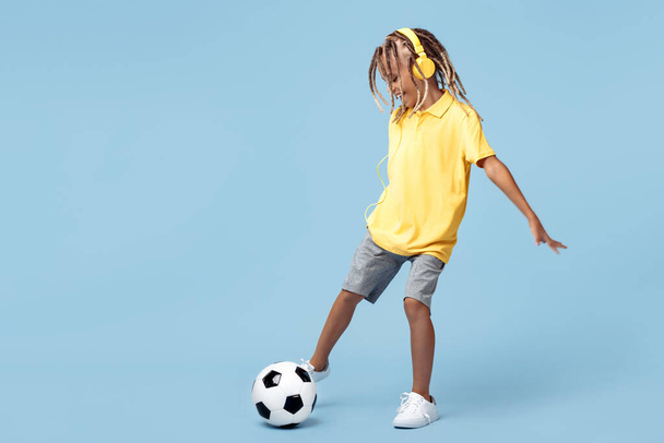 Sporty little boy with african dreads shoot soccer ball over blue background - Photo, Image
