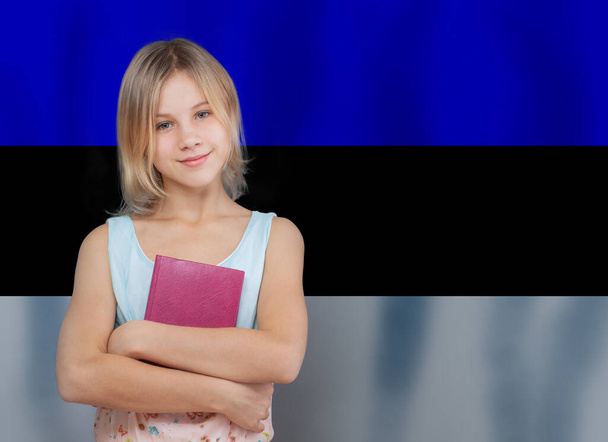 Милая девочка-подросток держит книгу на фоне эстонского флага - Фото, изображение
