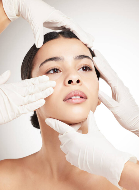 Beautiful young woman having her face examined against a grey studio background. Hispanic female taking care of her skin with a checkup against a background. - Photo, Image