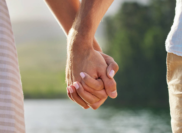 an unrecognizable couple holding hands while spending time at a lake. - Foto, Bild