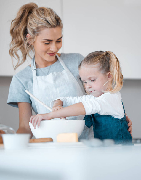 Boldog anya segít a gyerekének sütni. A nő, aki a lányát nézi sütni. Kaukázusi kislány kevert egy tál tésztát. Büszke anya nézi, ahogy a lánya süt. Kislány élvezi a sütést. - Fotó, kép