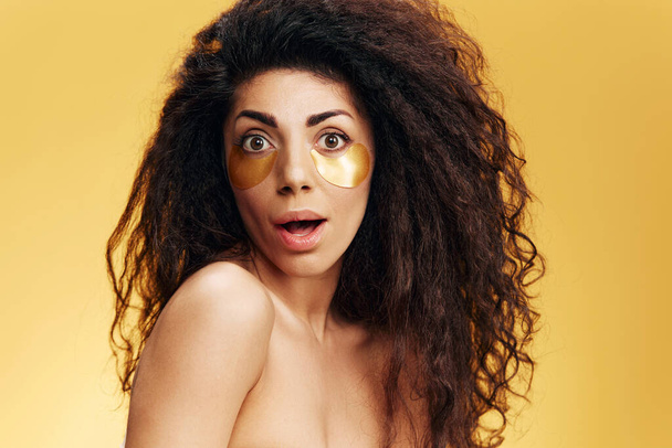 驚いたことに,目の下に黒いヒドロゲルパッチが付いているかなりラテン語の女性は,黄色の背景の上に隔離された口を開きました. 化粧品 広告 自然 美 コンセプト スタジオ ポートレート コピー スペース - 写真・画像