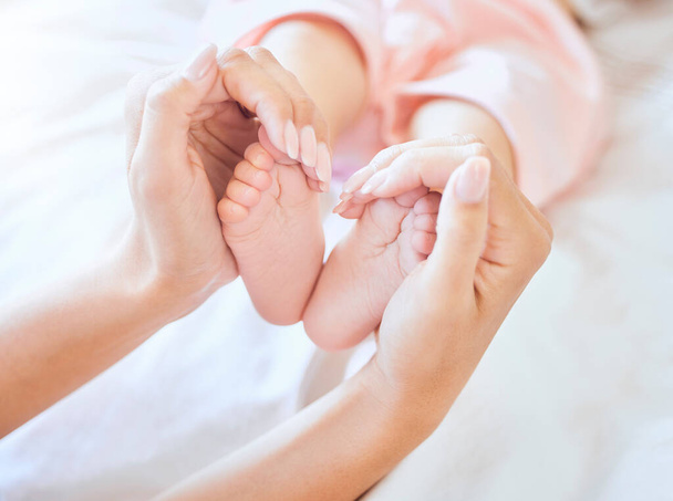 Mother holding baby feet. Closeup of tiny newborn baby feet held by a parent. Small baby toes. Little baby lying on a bed. Woman holding feet of little baby girl. Innocent infant being held by mother. - Zdjęcie, obraz