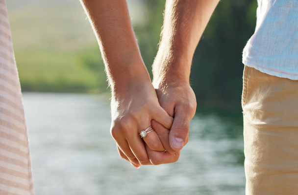 an unrecognizable couple holding hands while spending time at a lake. - Foto, imagen