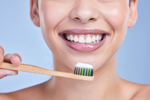 Closeup of a smiling mixed race young woman with glowing skin posing against blue copyspace background while brushing her teeth for fresh breath. Hispanic model using toothpaste to prevent a cavity. - Foto, Imagen