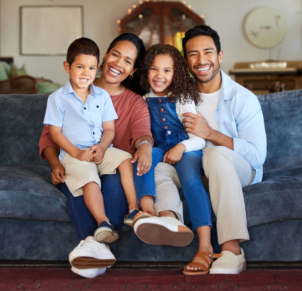 Happy family with two children sitting at home. Happy mixed race family close together on sofa at home. Cheerful mother, father and little children smiling and looking at camera. - Photo, Image